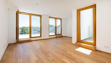 Helles, leeres Wohnzimmer mit Holzboden und Zugang zu mehreren Balkonen.