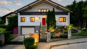 Modernes Einfamilienhaus mit gepflegtem Vorgarten, beleuchtetem Eingangsbereich und Garage.