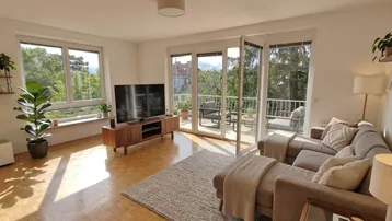 Helles Wohnzimmer mit Parkettboden, großem Sofa und Zugang zum möblierten Balkon.