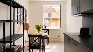 Moderne Küchenzeile mit schwarzen Schränken und Essbereich, hell durch ein Fenster mit Blick auf ein Nachbargebäude.