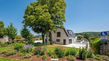 Modernes Einfamilienhaus mit gepflegtem Garten, großen Bäumen und weitem Blick ins Grüne.