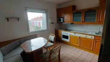 Gemütliche Wohnküche mit Holzeinbauten, Essbereich und Fensterblick nach draußen.