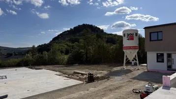 Baustelle des Neubaus mit Blick auf die umliegende grüne Hügellandschaft unter blauem Himmel.