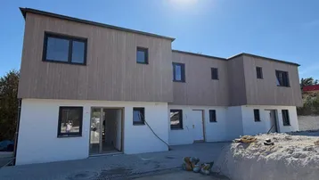 Neubau mit moderner Holzfassade und weißem Putz unter strahlendem Sonnenschein.