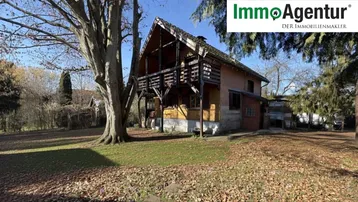 Charmantes Holzhaus im Chalet-Stil mit Balkon und großem Garten unter blauem Himmel.
