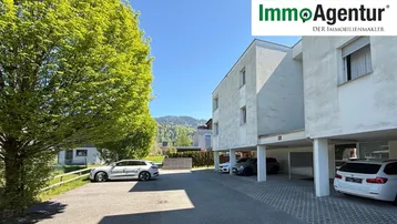 Moderne Wohnanlage mit Carports und Außenparkplätzen vor bergiger Kulisse.