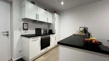 Moderne Einbauküche mit weißen Schränken, schwarzen Arbeitsplatten und integrierten Geräten.