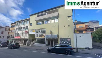 Mehrstöckiges Gebäude mit Geschäften im Erdgeschoss und Wohnungen darüber, an einer belebten Straße gelegen.