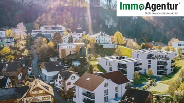 Luftaufnahme moderner Wohngebäude mit Balkonen vor einer malerischen Bergkulisse.