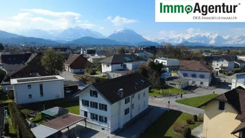 Luftaufnahme des Hauses mit umliegender Nachbarschaft und beeindruckendem Alpenpanorama im Hintergrund.