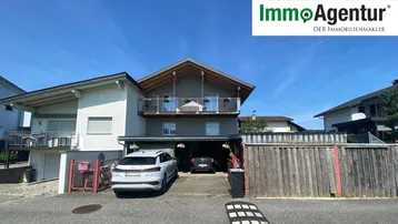 Ansicht des Hauses von vorne mit Carport und Balkon unter blauem Himmel.