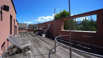 Geräumige Dachterrasse mit Holzdeck, Liegestühlen und weitem Blick auf die umliegende Berglandschaft.