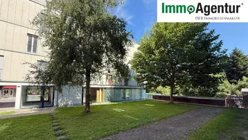 Mehrfamilienhaus mit Grünfläche und Bäumen im Vordergrund, an einem sonnigen Tag.