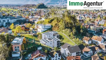 Luftaufnahme einer Wohngegend mit modernen Gebäuden und beeindruckendem Alpenpanorama im Hintergrund.
