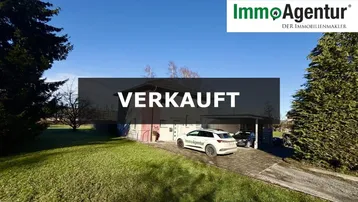 Außenansicht eines Einfamilienhauses mit großem Rasen, Einfahrt und Carport unter blauem Himmel.