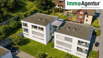 Moderne weiße Wohngebäude mit Flachdächern und grüner Umgebung, eingebettet in eine Wohnsiedlung.