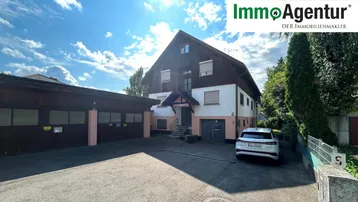 Großes Wohnhaus mit Satteldach, angrenzender Garage und Stellplätzen im Freien.