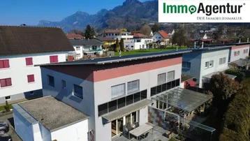 Luftaufnahme des modernen Wohnhauses mit Garten und umliegender Berglandschaft an einem sonnigen Tag.