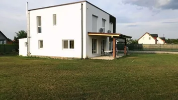 Modernes Einfamilienhaus mit weißer Fassade, großer Rasenfläche und überdachter Terrasse.