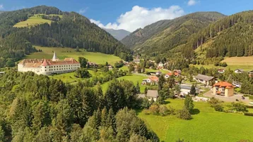 Malerisches Dorf in einem grünen Tal mit historischen Gebäuden und bewaldeten Bergen im Hintergrund.