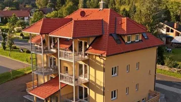 Modernes Mehrfamilienhaus mit mehreren Balkonen und rotem Ziegeldach in alpiner Umgebung.