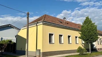 Seitenansicht des Hauses mit gelber Fassade, Ziegeldach und mehreren Fenstern.