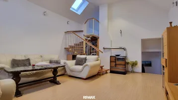 Geräumiges Wohnzimmer mit gemütlicher Sitzecke, traditionellem Ofen und Treppe zum Obergeschoss mit Dachfenster.