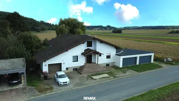 Freistehendes Einfamilienhaus mit Doppelgarage und Carport, umgeben von Feldern und grüner Landschaft.