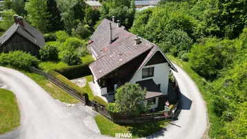 Luftaufnahme eines Hauses an einer Kurve, umgeben von Bäumen und einem gepflegten Garten.