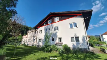 Mehrstöckiges Gebäude mit weißer Fassade und Gartenbereich unter blauem Himmel.