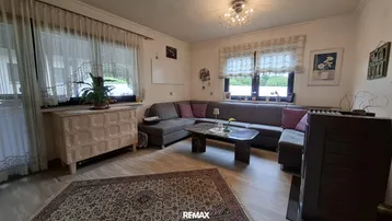 Gemütliches Wohnzimmer mit großem Ecksofa, Teppich und hellen Fenstern.