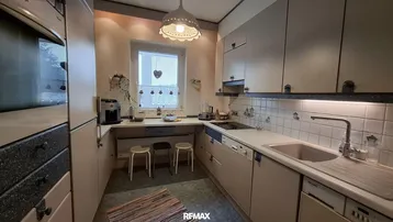 Funktionale Küche mit hellen Schränken, Fliesenrückwand und Fenster über der Arbeitsplatte.