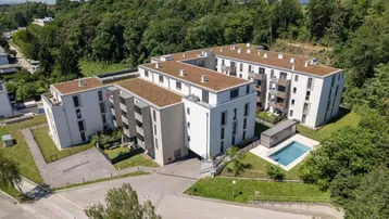 Moderne Wohnanlage mit begrünten Flachdächern und Gemeinschaftspool, umgeben von viel Grün.