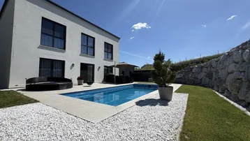 Modernes Haus mit privatem Pool, Whirlpool und gepflegtem Gartenbereich unter blauem Himmel.