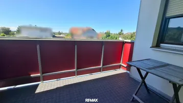 Kleiner Balkon mit roter Verkleidung und Tisch, ideal für eine Kaffeepause.