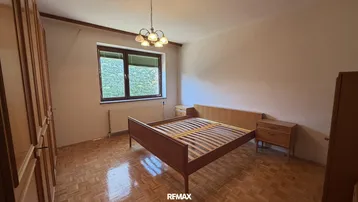 Helles Schlafzimmer mit Parkettboden, einem Doppelbett und einem Fenster mit Blick ins Grüne.
