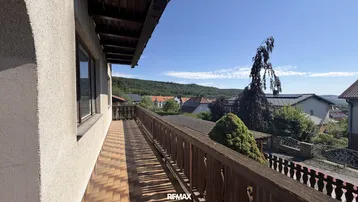 Langer Balkon mit Fliesenboden und Holzgeländer, der einen weiten Blick über die Landschaft bietet.