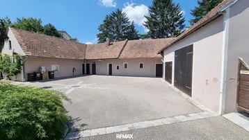 Großer Innenhof umgeben von Gebäuden mit traditionellen Ziegeldächern unter blauem Himmel.