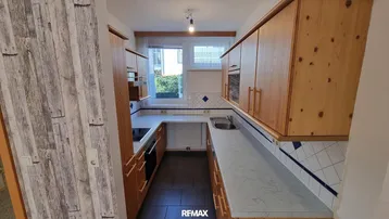 Funktionale Küche mit Holzschränken, hellen Arbeitsplatten und blauen Fliesen als Spritzschutz.