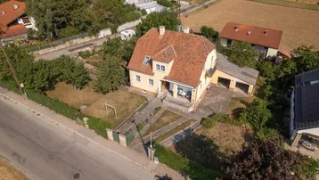 Luftaufnahme eines Einfamilienhauses mit rotem Ziegeldach und angrenzender Garage in ländlicher Umgebung.