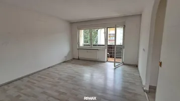 Helles Zimmer mit Laminatboden und Zugang zu einem kleinen Balkon.