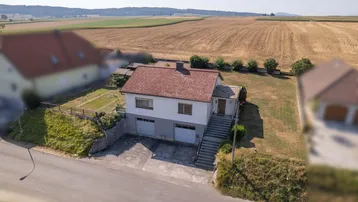 Luftaufnahme eines Einfamilienhauses mit rotem Ziegeldach, Doppelgarage und weiten Feldern im Hintergrund.