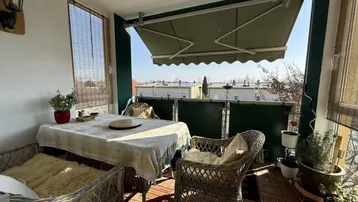 Möblierter Balkon mit Markise, Holzboden und Blick auf die Umgebung.