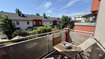 Sonniger Balkon mit Holzboden und Sitzgelegenheiten, bietet Blick auf die Nachbarschaft.