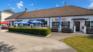 Außenansicht des Gasthauses mit einladender Terrasse und Sonnenschirmen unter blauem Himmel.