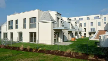 Moderne Wohnanlage mit weißer Fassade, Balkonen und gepflegter Rasenfläche unter blauem Himmel.