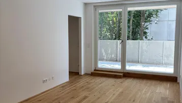 Heller Raum mit neuem Parkettboden, weißen Wänden und Zugang zu einer Terrasse.