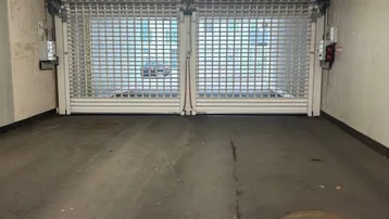 Einfahrt zur Tiefgarage mit robustem Rolltor und Betonwänden.