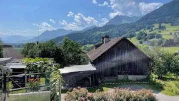 Idyllischer Blick auf eine ländliche Landschaft mit Bergen und einem traditionellen Holzhaus.