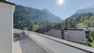 Sonnige Dachterrasse mit Fliesenboden, Gartenmöbeln und beeindruckendem Bergblick.